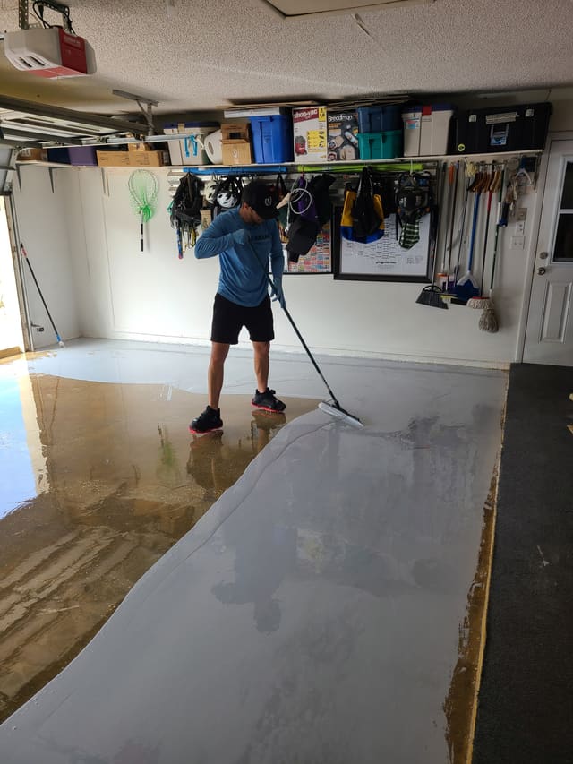 Installer applying a gray base coat across a prepared residential garage floor.
