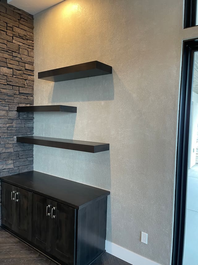 Floating shelves with a dark decorative coating against an accent wall.