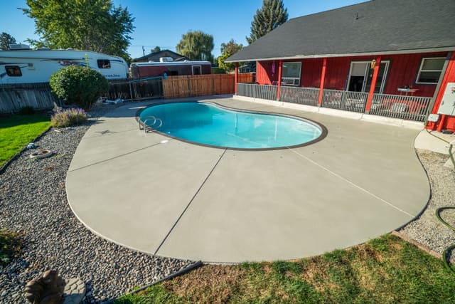 Backyard pool deck and patio concrete with a light outdoor coating.