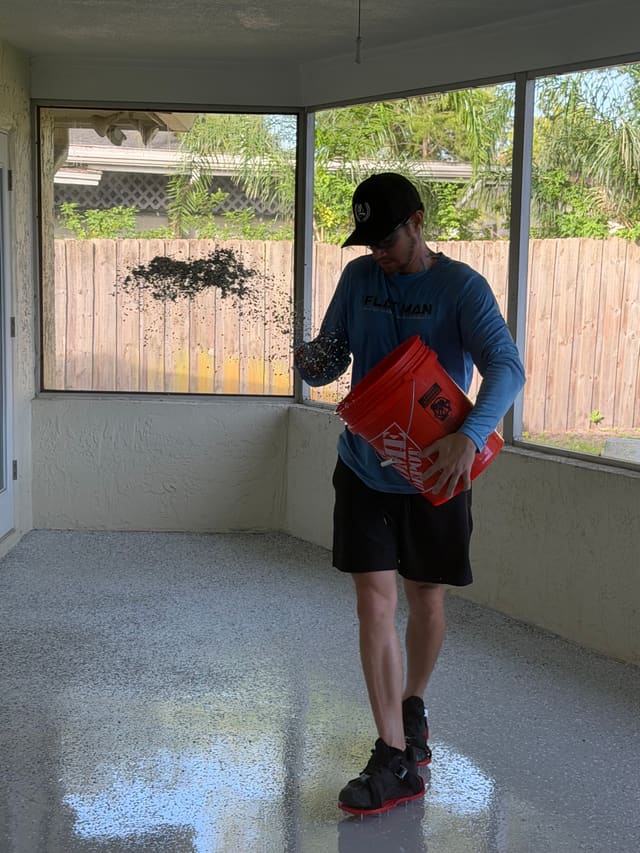 Installer broadcasting decorative flakes over a coated screened patio floor.